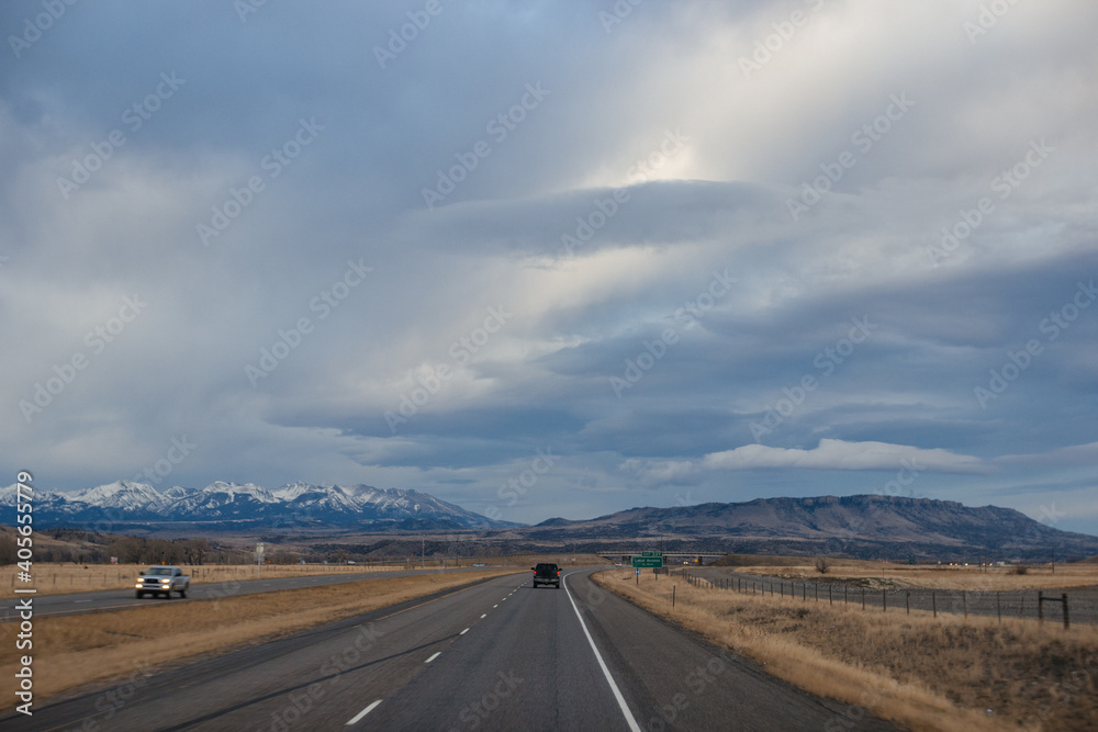 Asphalt road among steppes with yellow dry grass, blue mountains on the horizon, beautiful blue-gray autumn sky. Montana, USA, 11-23-2019