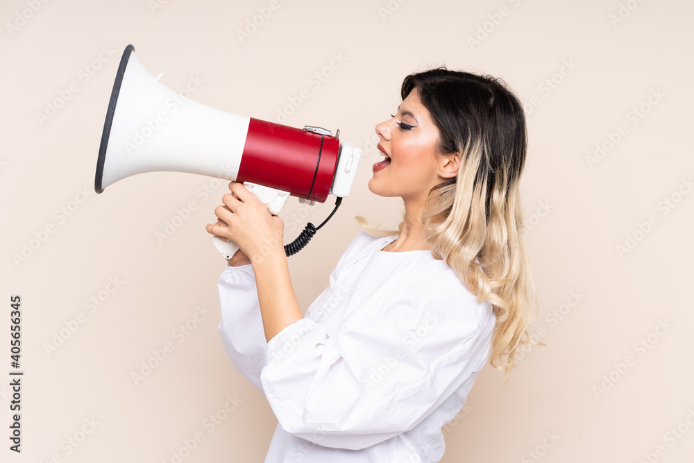 Teenager girl isolated on beige background shouting through a megaphone Teenager girl isolated on beige background shouting through a megaphone