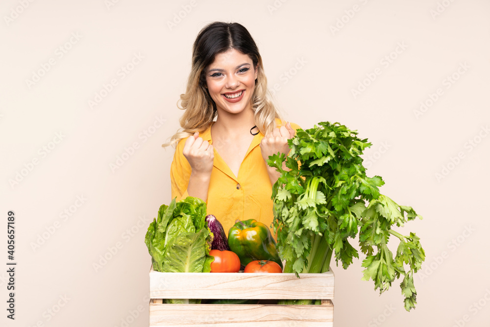 Teenager farmer girl with freshly picked vegetables in a box isolated on beige background celebrating a victory Teenager farmer girl with freshly picked vegetables in a box isolated on beige background celebrating a victory