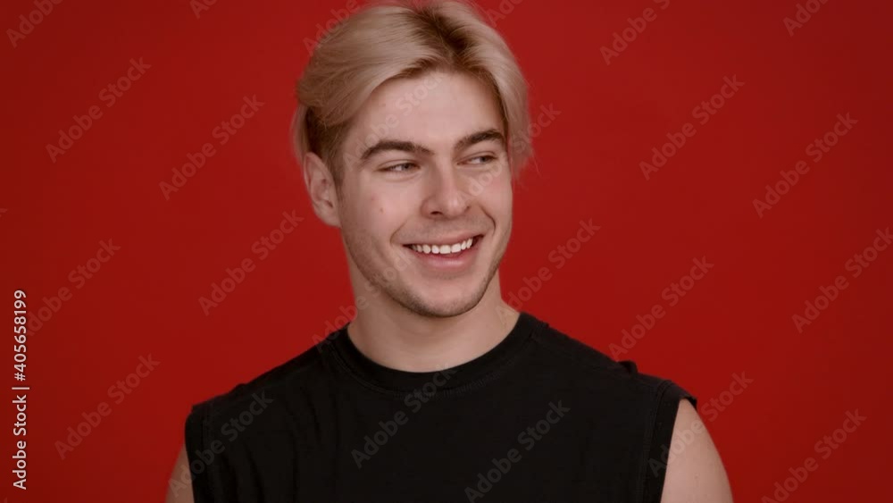 Close up studio portrait of happy blonde guy laughing at camera, red background, slow motion Close up studio portrait of happy blonde guy laughing at camera, red background, slow motion