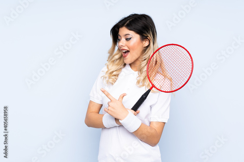 Teenager girl playing badminton isolated on blue background pointing finger to the side © luismolinero