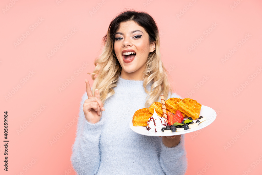 Teenager girl holding waffles on isolated pink background pointing up a great idea