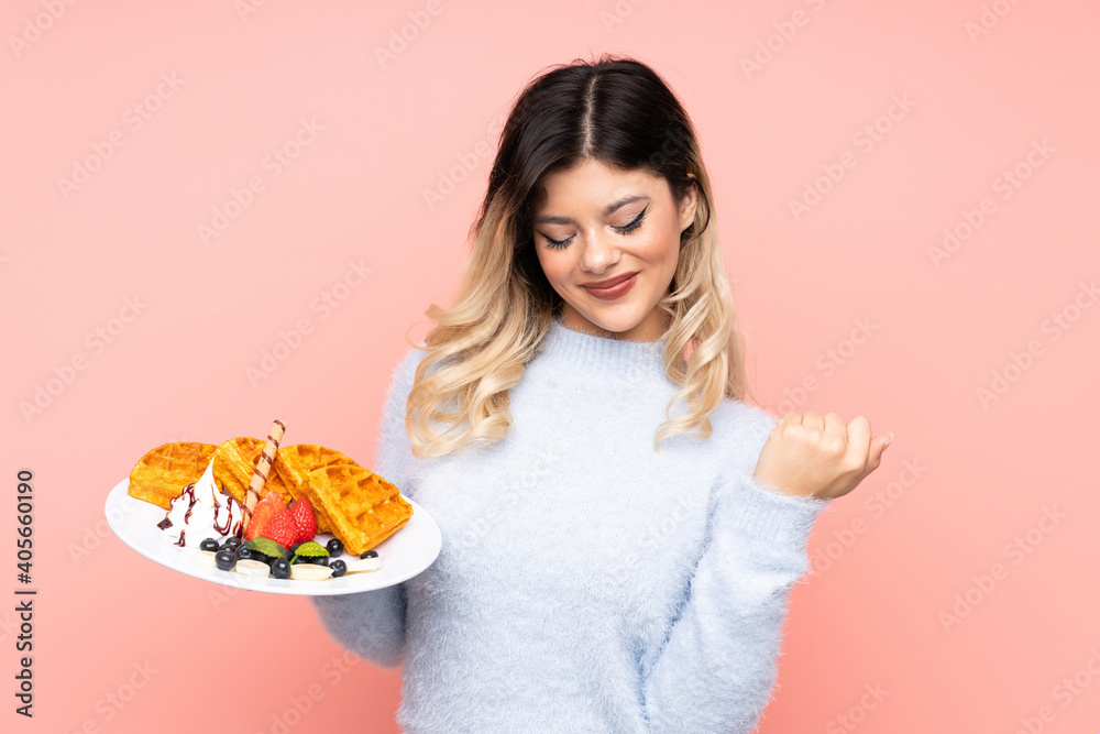 Teenager girl holding waffles on isolated pink background celebrating a victory Teenager girl holding waffles on isolated pink background celebrating a victory