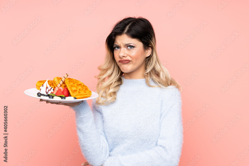 Teenager girl holding waffles on isolated pink background with sad expression