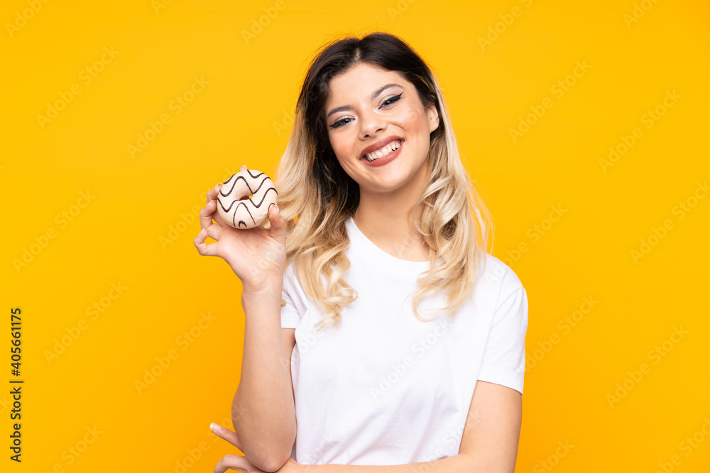 Teenager girl isolated on yellow background holding a donut and happy Teenager girl isolated on yellow background holding a donut and happy