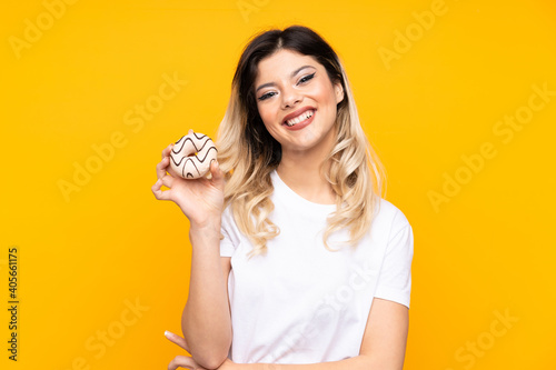 Teenager girl isolated on yellow background holding a donut and happy