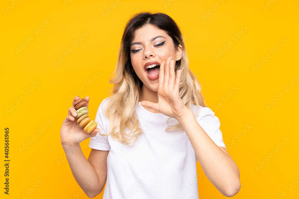 Teenager girl isolated on yellow background holding colorful French macarons and shouting Teenager girl isolated on yellow background holding colorful French macarons and shouting