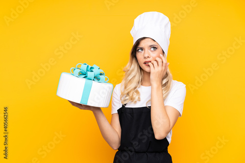 Teenager girl pastry holding a big cake isolated on yellow background nervous and scared