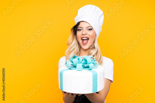 Teenager girl pastry holding a big cake isolated on yellow background