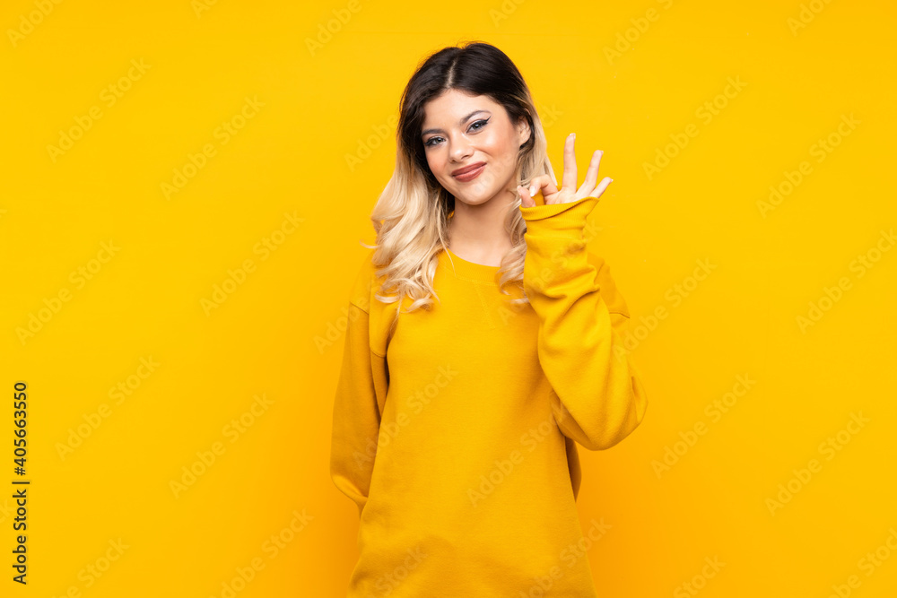 Teenager girl isolated on yellow background showing ok sign with fingers