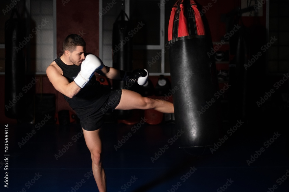 Muscular handsome kickboxing fighter giving a forceful kick during a practise round with a boxing bag. High quality photo
