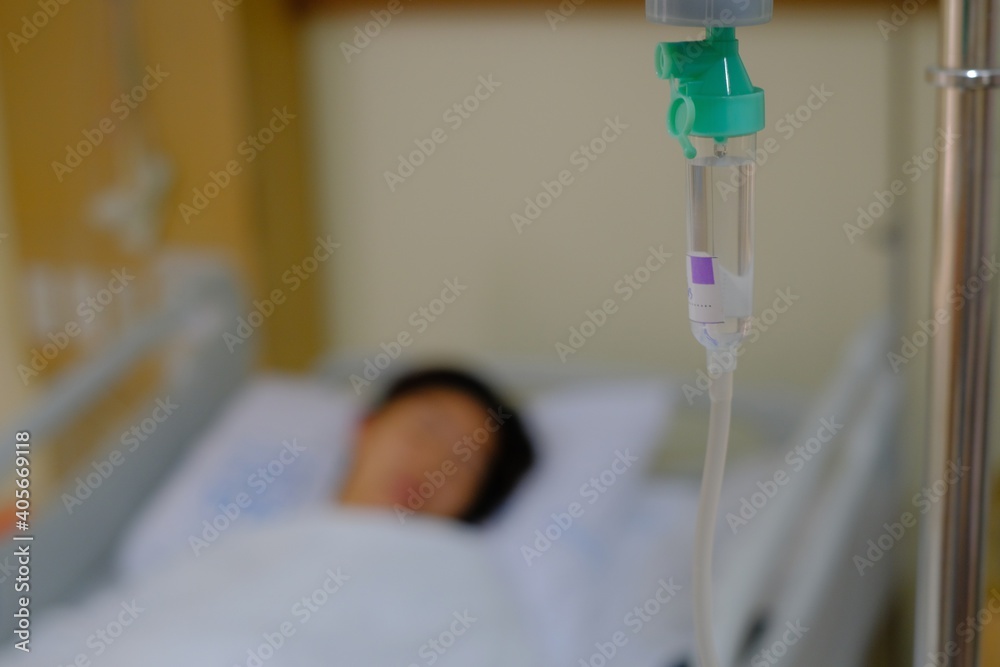 An out of focus picture of a woman resting in her hospital bed after a surgery, sleeping with an iv line dripping saline and medicine to her vein.