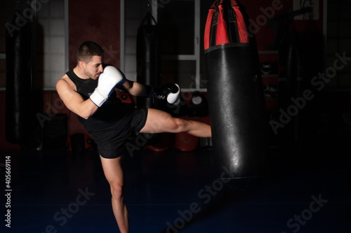 Muscular handsome kickboxing fighter giving a forceful kick during a practise round with a boxing bag. High quality photo © herraez