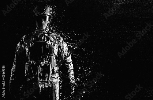 Foto Black and white photo of a fully equipped soldier standing in tactical clothing and dissolving on grungy black background