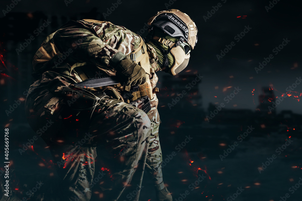 Photo of a fully equipped soldier in armored vest, helmet, face glasses and protection kneeling and attacking with knife on shaded destructed city background.