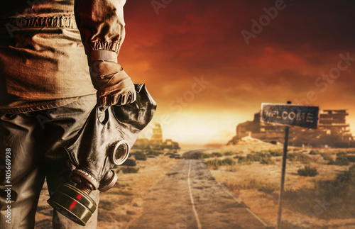 Photo of a stalker in jacket and gloves holding gas mask with filter on destructed apocalyptic wasteland city background.