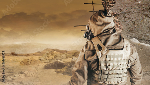 Photo of a stalker in jacket, armored vest standing back view in soviet gas mask with filter on destructed apocalyptic desert wasteland background.