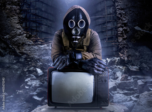 Photo of stalker soldier in jacket and armored vest and rubber gloves standing with old tv set on ruined dark background. photo