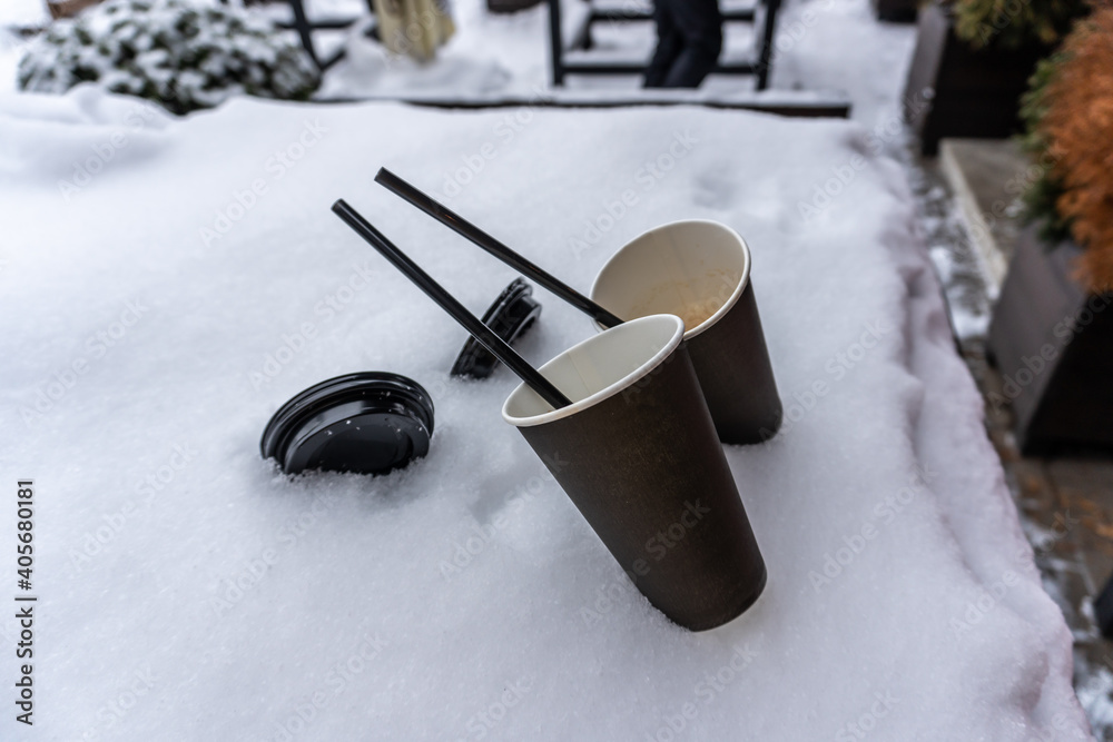 Two coffee cups and straws stick out in the snow on the terrace next to the street cafe Two coffee cups and straws stick out in the snow on the terrace next to the street cafe