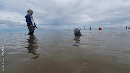 January 2021, Balikpapan Indonesia, lamaru beach, people enjoys calm ocean waves, muslim mother teach her daughter to swim photo