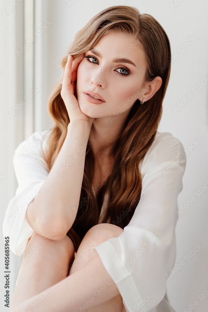 beautiful woman in white robe sits on windowsill.morning of bride before wedding beautiful woman in white robe sits on windowsill.morning of bride before wedding