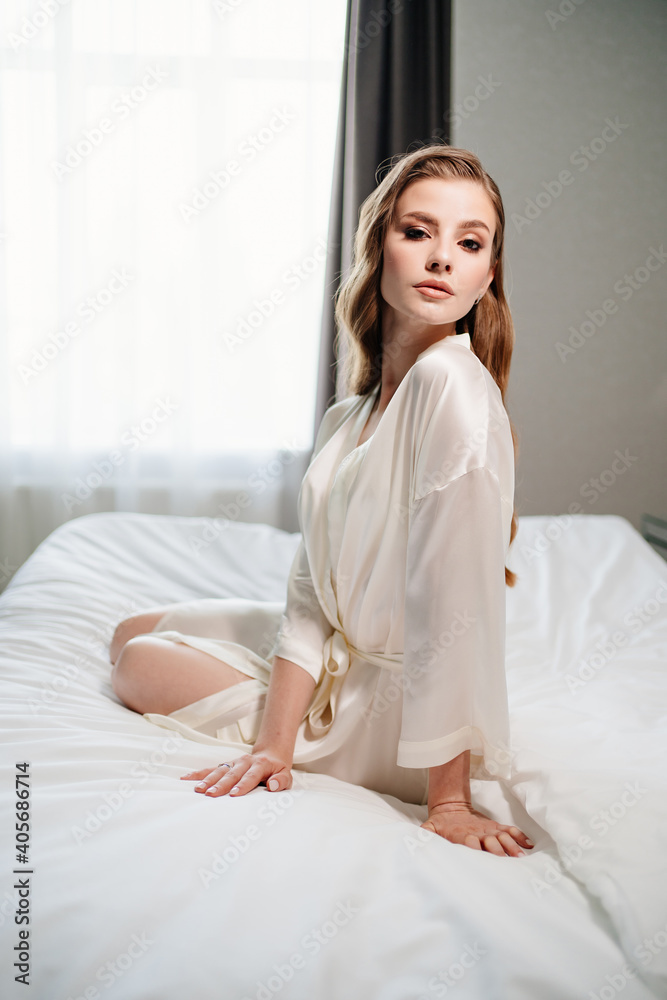 beautiful woman with makeup, long hair sits in white robe on bed beautiful woman with makeup, long hair sits in white robe on bed