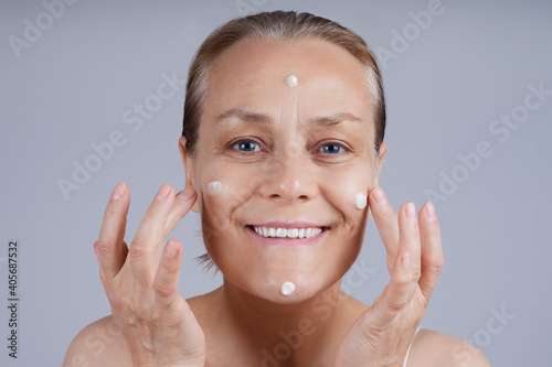 Happy senior apply cosmetic cream to her face. Face skincare in older age.