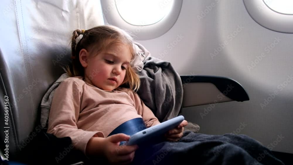 Child in airplane. Kid with mobile phone in air plane in window seat. Flight entertainment for kids. Traveling with young children. Kids fly and travel. Family vacation Child in airplane. Kid with mobile phone in air plane in window seat. Flight entertainment for kids. Traveling with young children. Kids fly and travel. Family vacation