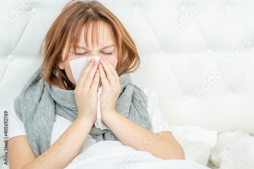 Diseased girl sitting on the bed and blowing her nose in tissue