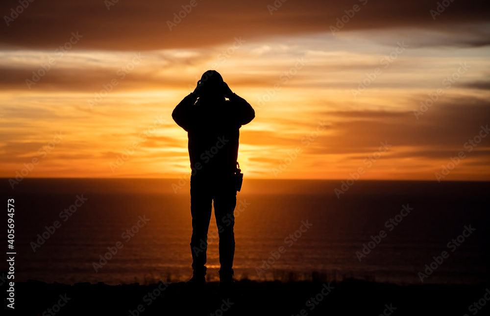 Silhouette of a man looking out over the ocean at sunset