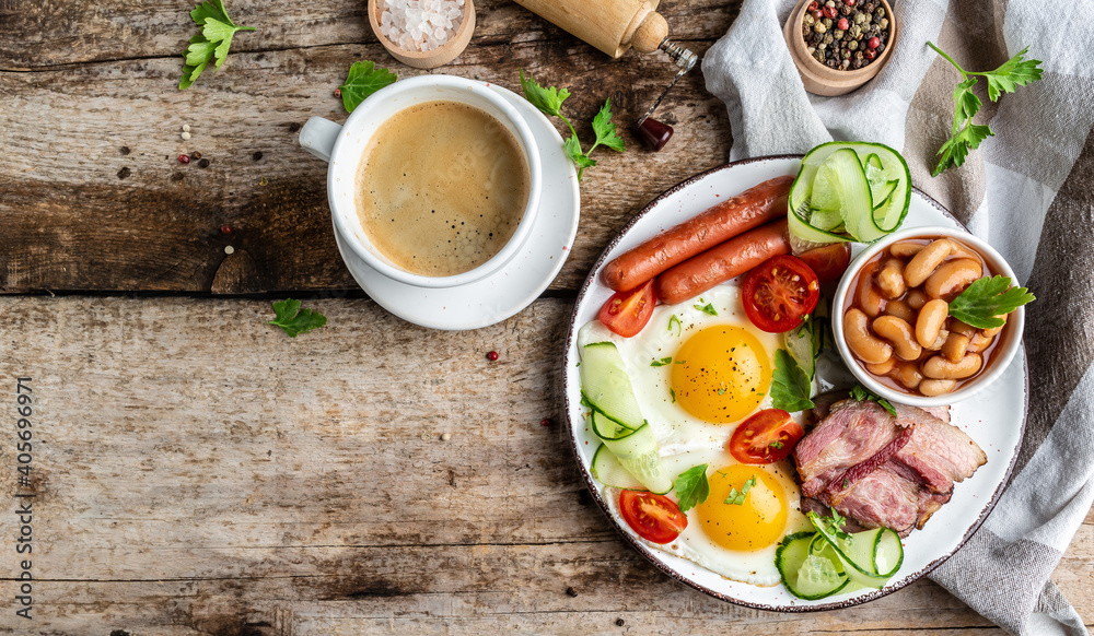 English breakfast. Fried eggs, sausages, bacon, beans, tomatoes and coffee cup on wooden table. Top view. copy space English breakfast. Fried eggs, sausages, bacon, beans, tomatoes and coffee cup on wooden table. Top view. copy space