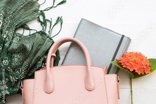 green scarf with pink handbag ,notebook planner for lifestyle woman and orange flowers spike flora of asia arrangement flat lay style on background white 
