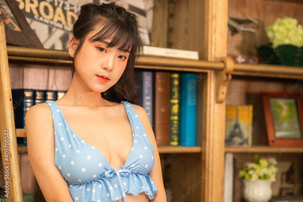 A beautiful, sexy woman. She is an Asian Thai in a polka dot blue lingerie. She is standing at the bookshelves in the library.