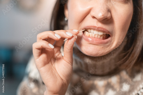 Asian woman has a toothache after a big meal and she pulls out the remains of food from the cavity in her teeth with a toothpick. The concept of dental health and cleaning photo