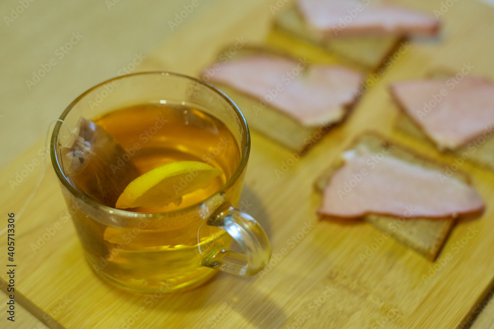 a cup of tea with lemon and rye bread with ham on a wooden board a cup of tea with lemon and rye bread with ham on a wooden board