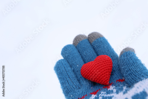 Red heart on palm of hand in warm knitted glove against the snow. Concept of a romantic love, Valentine's day or charity