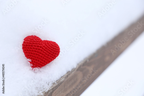 Valentine heart in a snow on wooden bench. Red knitted symbol of love  background for winter holiday