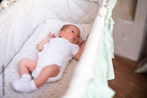 Newborn baby boy in bed. New born child in white bodykit lying in light cradle. Children sleep. Bedding for kids. Infant napping in bed. Healthy little kid shortly after birth © Lena May