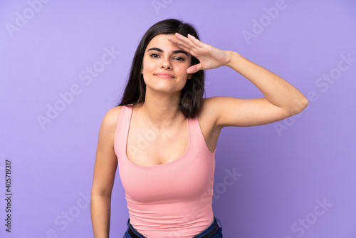 Young woman over isolated purple background looking far away with hand to look something