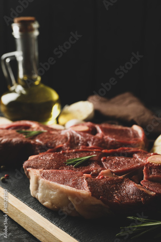 Board with raw steak meat, herbs and spices on black smokey background