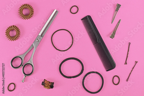 Hair styling concept with elastic hair ties, hair pins, comb and thinning shears on pink background