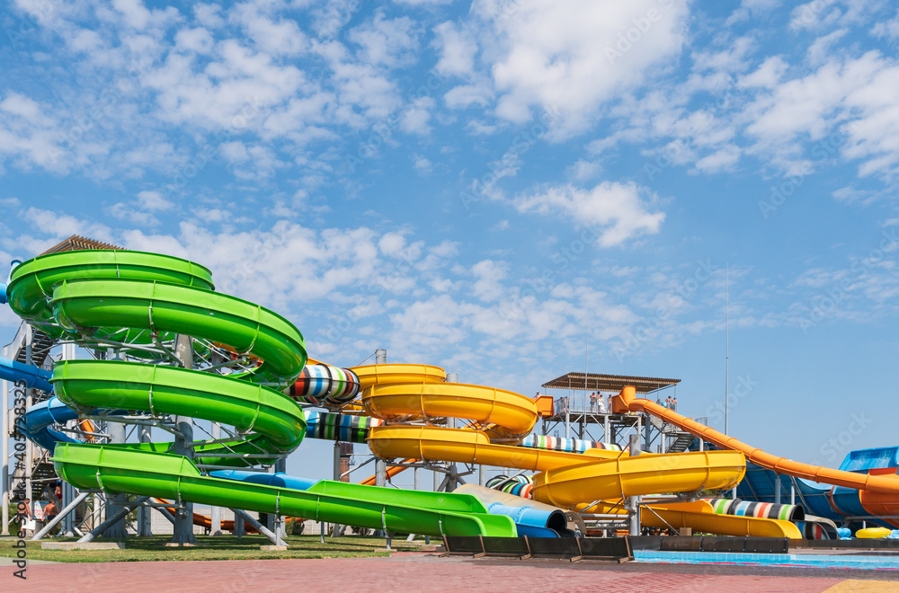 Water park, bright multi-colored slides with a pool. A water park without people on a summer day with a beautiful, cloudy blue sky Water park, bright multi-colored slides with a pool. A water park without people on a summer day with a beautiful, cloudy blue sky