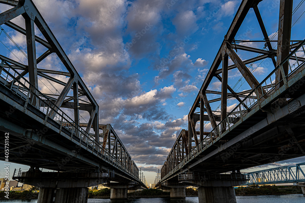 Two rail roads are running in parallel under blue sky and beautiful clouds.  The bridges are rusted and showing legacy products. 