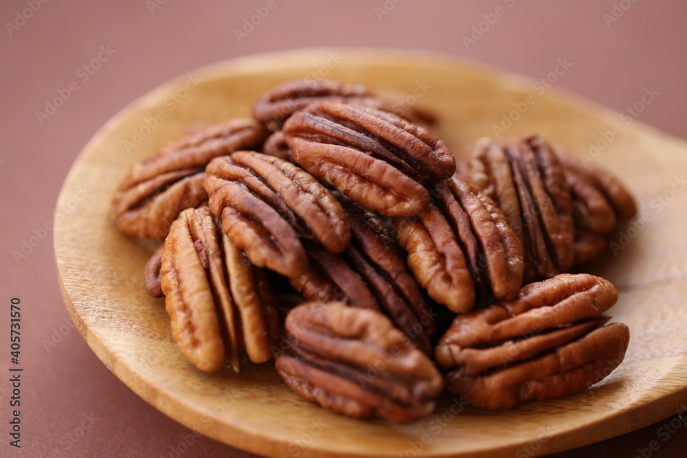 Pecan nut close-up in wooden spoon on bright brown background.Healthy fats.Heap shelled Pecans nut closeup. Tasty raw organic food and healthy snack