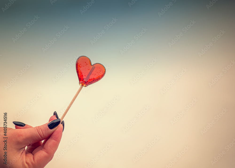 Heart shaped lollipop held in hand on yellow blue background, love, valentine's day