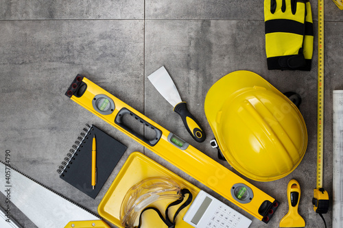 Contractor concept. Tool kit of the contractor: yellow hardhat, libella, hand saw on the gray tiles background. © zolnierek