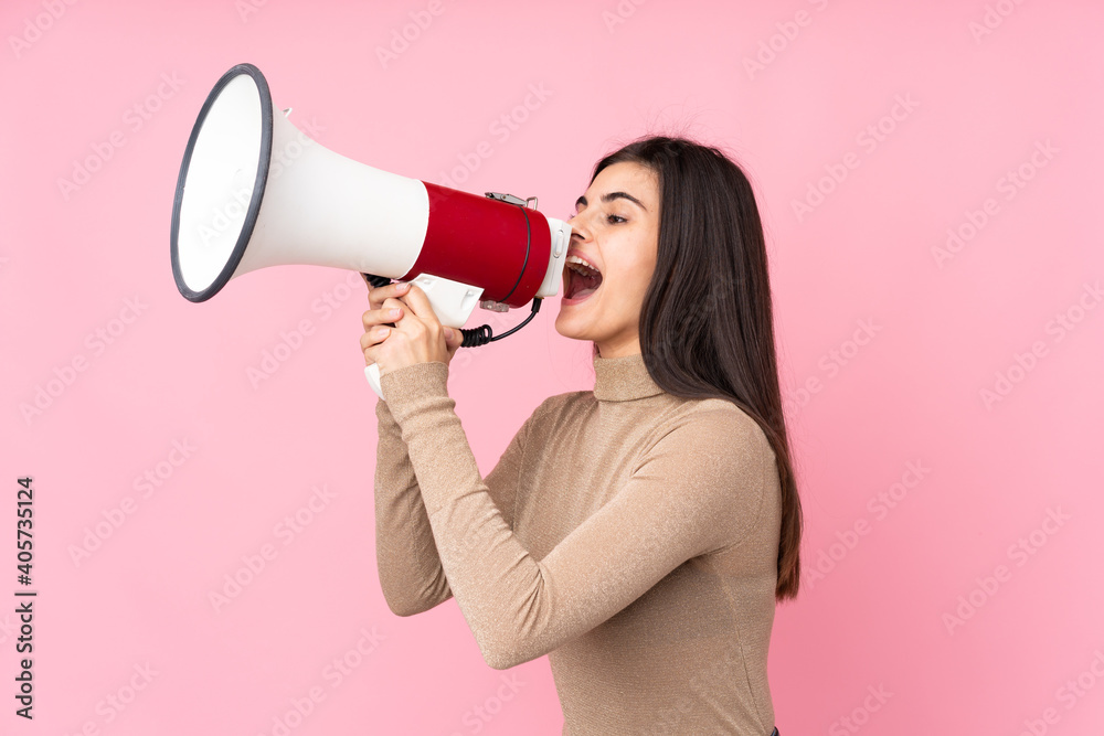 Young woman over isolated pink background shouting through a megaphone Young woman over isolated pink background shouting through a megaphone