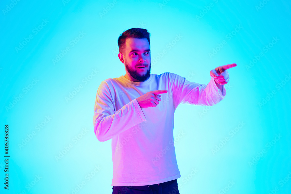Naklejka premium Pointing, choosing. Caucasian man's portrait isolated on blue studio background in neon light. Beautiful male model. Concept of human emotions, facial expression, sales, ad. Copyspace for ad.