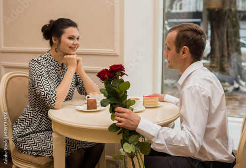 the lovers are sitting at a table in a cafe with a bouquet of roses. Focus on a bouquet of red roses