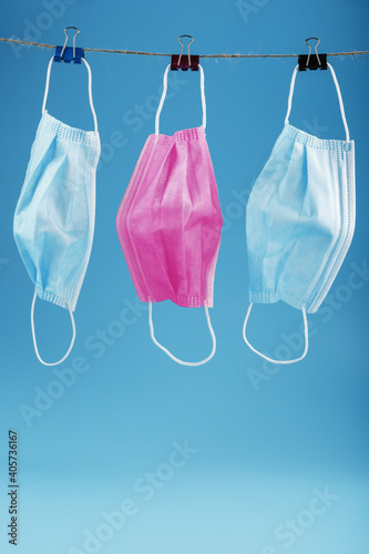 Three medical masks hanging on a rope, pink and blue on a blue background.